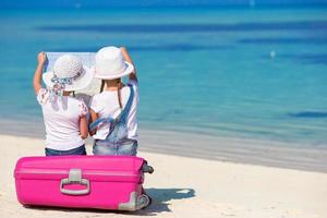 weinig meisjes met groot koffer en kaart Bij tropisch strand foto