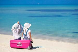 weinig meisjes met groot koffer en kaart Bij tropisch strand foto