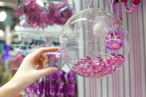 vrouw Holding Kerstmis glas kom met klein roze ballen Bij op te slaan foto