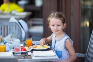 schattig klein meisje aan het ontbijt op terras foto