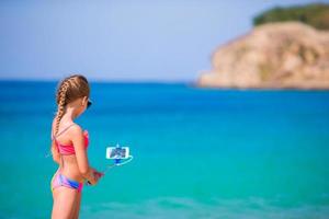 weinig meisje nemen zelfportret door mobiele telefoon Aan de strand. kind genieten van haar suumer vakantie en maken foto's achtergrond de zee foto