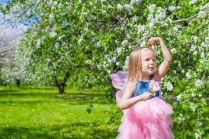 aanbiddelijk weinig meisje in bloeiend appel boom tuin Aan voorjaar dag foto