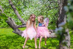 weinig aanbiddelijk meisjes zittend Aan bloeiende boom in appel tuin foto