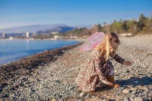 aanbiddelijk weinig meisje spelen Aan de strand in een winter zonnig dag foto