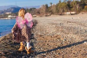 aantrekkelijk weinig meisje Aan de strand in een pak met vlinder Vleugels foto