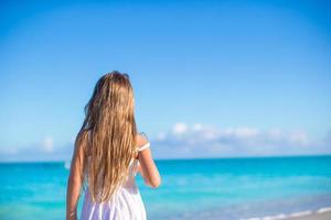 terug visie van aanbiddelijk weinig meisje Bij wit strand gedurende zomer vakantie foto