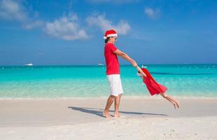 weinig meisje en gelukkig vader in de kerstman hoed hebben pret Bij tropisch strand foto