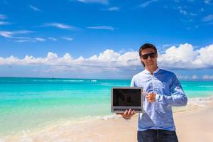 jong Mens met laptop Aan de achtergrond van turkoois oceaan Bij tropisch strand foto