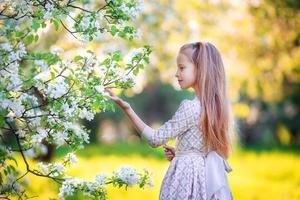 aanbiddelijk weinig meisje in bloeiend appel boom tuin Aan voorjaar dag foto