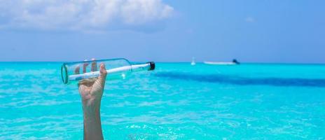 fles met een bericht in de hand- achtergrond blauw lucht foto