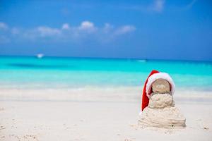 weinig zanderig sneeuwman met rood de kerstman hoed Aan wit caraïben strand foto