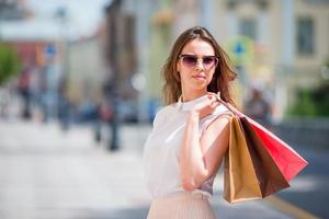 jong gelukkig meisje met boodschappen doen Tassen buitenshuis. portret van een mooi gelukkig vrouw staand Aan de straat Holding boodschappen doen Tassen glimlachen foto