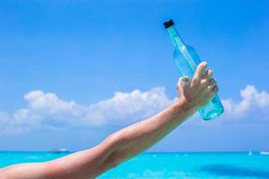 fles met een bericht in de hand- achtergrond blauw lucht foto