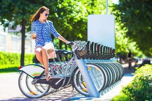 jong vrouw met glas van koffie Aan fiets buitenshuis foto