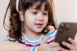 een schattig weinig meisje is verloofd met een leraar online door telefoon. online onderwijs van kinderen. kleuters en gadgets. hoog kwaliteit foto