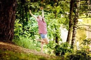 mooi jong meisje in een plaid overhemd en kort denim shorts in vastpinnen stijl blijft in water van rivier- foto