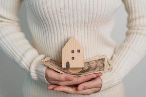 vrouw Holding Japans yen bankbiljet en huis model. echt landgoed, huis, hypotheek, Japan contant geld, belasting, recessie economie, inflatie, investering, financiën en spaargeld concepten foto