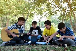 Aziatisch jong tieners zittend samen, praten, lezing, overleg plegen en spelen de quitar Aan weekend in de park, zacht en selectief focus. foto