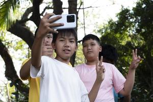 groep van jong Aziatisch tiener jongens uitgeven vrij keer in de park razen hun vingers en nemen selfie samen gelukkig, zacht en selectief focus Aan jongen in wit t-shirt, verhogen tieners concept. foto