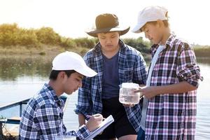 jong Aziatisch jongen houdt transparant buis welke heeft voorbeeld water binnen naar Doen de experiment en ph niveau meting net zo zijn school- project werk met zijn vrienden achter Bij de rivier- waar hij leefde. foto