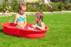 twee weinig zussen spelen en spatten in de zwembad Aan een heet zonnig dag foto