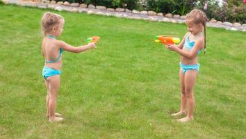 twee weinig aanbiddelijk meisjes spelen met water geweren in de werf foto