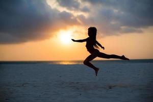 silhouet van aanbiddelijk weinig meisje Aan wit strand Bij zonsondergang foto