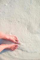 vrouw voeten Aan de wit zand strand in Ondiep water foto