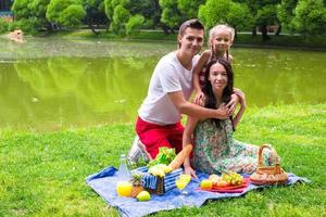 gelukkige jonge familie picknicken buiten in de buurt van het meer foto