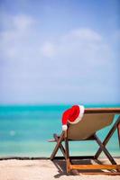 rood de kerstman hoed Aan strand stoel Bij tropisch vakantie foto