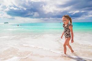 aanbiddelijk weinig meisje hebben pret Bij Ondiep water Aan wit strand foto