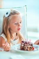 weinig meisje vieren gelukkig verjaardag met smakelijk taart in buitenshuis cafe foto