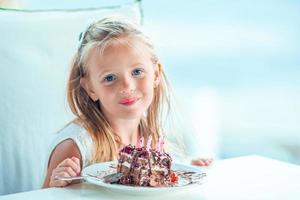 weinig meisje vieren gelukkig verjaardag met smakelijk taart in buitenshuis cafe foto