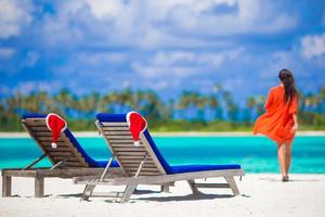 twee ligstoelen met rood de kerstman hoeden Aan tropisch wit strand met turkoois water foto