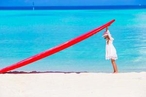 aanbiddelijk weinig meisje met rood groot surfboard Aan tropisch wit strand foto