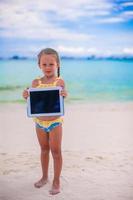 weinig meisje Holding laptop Aan strand foto