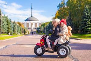 twee weinig mooi zussen zittend Aan speelgoed- motorfiets in groot park foto