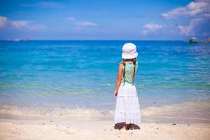 achterzijde visie van weinig meisje in hoed op zoek Bij de zee Aan wit zand strand foto