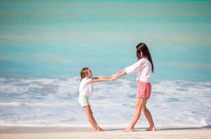 familie pret Aan wit zand. glimlachen moeder en aanbiddelijk kind spelen Bij zanderig strand Aan een zonnig dag foto