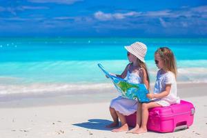 weinig meisjes met groot koffer en kaart Aan tropisch strand foto