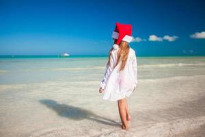 weinig schattig meisje in rood hoed de kerstman claus Aan de strand foto