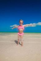 weinig meisje verspreiding haar armen staand Bij de wit strand foto