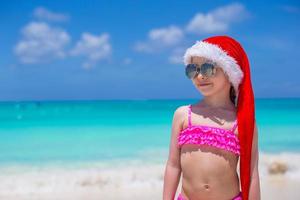 weinig schattig meisje in rood hoed de kerstman claus Aan de strand foto