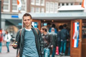 gelukkig Kaukasisch toerist met vers haring met ui en Nederland vlag in Amsterdam. traditioneel Nederlands voedsel buitenshuis foto