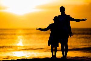 weinig meisje en gelukkig moeder silhouet in de zonsondergang Bij de strand foto