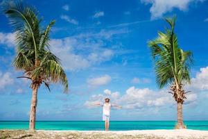 schattig weinig meisje in wit jurk Bij strand gedurende caraïben vakantie. aanbiddelijk baby staand tussen palm bomen Aan antigua eiland foto