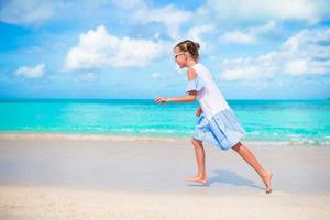 gelukkig weinig meisje rennen en spatten Bij Ondiep water Bij strand hebben een veel van pret Aan vakantie foto