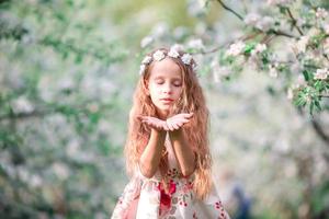 portret van aanbiddelijk weinig meisje in bloeiend kers boom tuin buitenshuis foto