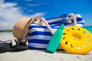 streep tas, rietje hoed, sunblock en frisbee Aan wit zanderig tropisch strand foto