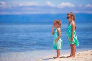 weinig aanbiddelijk meisjes in turkoois jurk Aan wit strand kijken Bij de zee foto